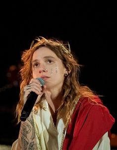 a woman with long hair and piercings on her face holding a microphone in front of her