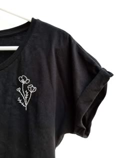 a black t - shirt with white flowers embroidered on the front and back, sitting on a hanger