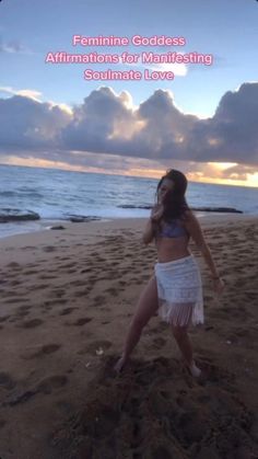 a woman standing on top of a sandy beach next to the ocean in front of clouds