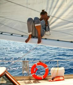 a woman sitting on the edge of a sailboat looking at the water while taking a photo