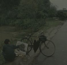 a man sitting on the side of a road next to a bike with an umbrella