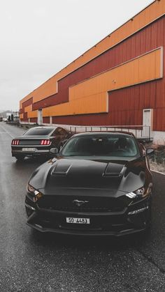 two black cars parked in front of a red building on the side of the road