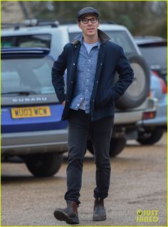 the young man is standing in front of his car wearing glasses and a blue jacket