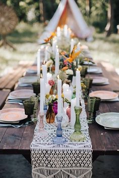 a long table is set with candles and plates on it for an outdoor dinner party