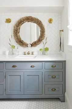 a bathroom with blue cabinets and a round mirror on the wall above it is decorated with gold accents