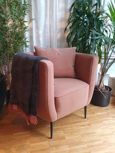 a pink chair sitting next to a potted plant on top of a hard wood floor