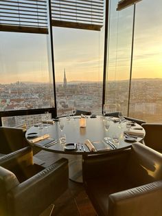 a round table with glasses and silverware in front of large windows overlooking the city