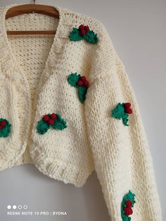 a white knitted sweater with holly decorations on it