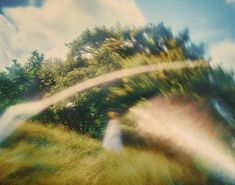 a blurry image of a woman in a white dress standing on a hill with trees behind her