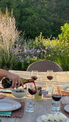 a person pouring wine into a bowl on top of a table with plates and glasses