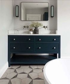 a white bath tub sitting next to a blue vanity with two sinks and mirrors above it