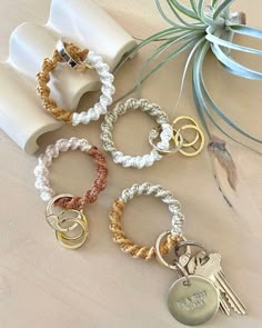 six different bracelets with key charms on top of a white cloth covered napkin next to an air plant