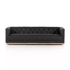 a black leather couch with wooden legs and buttons on the back, in front of a white background