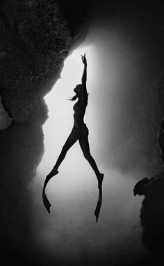 a woman jumping into the air from a cliff in black and white photo with light coming through