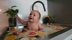 a baby sitting in a sink with lots of fruit