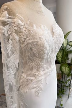 the back of a wedding dress on display in front of a potted green plant