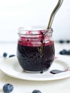 a glass jar filled with blueberry jam on top of a white plate next to a spoon