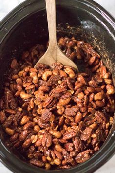 a wooden spoon in a slow cooker filled with nuts and meats, ready to be cooked