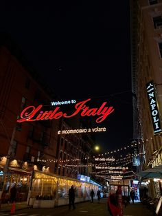 people are walking down the street in front of some buildings at night with lights on them