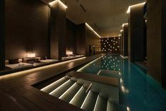 an indoor swimming pool surrounded by lounge chairs and lights on the walls, along with wooden flooring