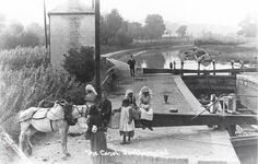 an old black and white photo of people standing near a horse drawn carriage on the side of a river