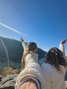 two people flying a kite on top of a mountain next to a body of water