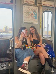 two women sitting on a subway train looking at their cell phones while they take pictures