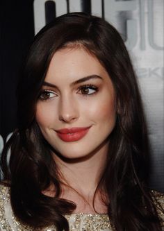 a close up of a person with long hair and brown eyes wearing a gold dress