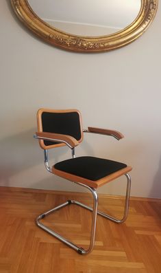 a chair sitting on top of a hard wood floor next to a gold framed mirror