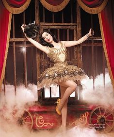 a woman in a gold and white dress is posing on a stage with her arms outstretched