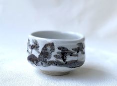 a small white and black cup sitting on top of a table next to a white sheet