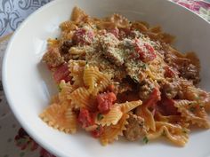 a white bowl filled with pasta covered in meat and tomato sauce on top of a table