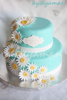 a three tiered cake with daisies on the top and bottom is blue, white and yellow