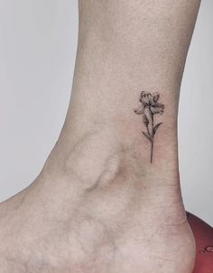 a small flower tattoo on the ankle is shown in black and grey ink, with a single white flower at the center