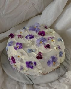 a cake with white frosting and purple pansies on it sitting on a marble platter