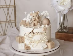 there is a white cake with gold letters and a teddy bear on the top it