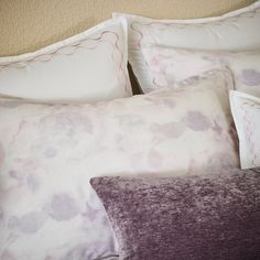 a close up of pillows on a bed with white sheets and purple pillowcases