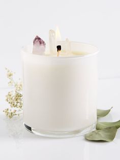 a candle with some rocks in it on a white surface next to flowers and leaves