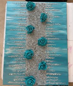 some blue flowers are sitting in the sand on a board that is painted with silver glitter