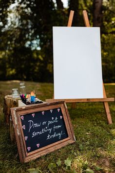 a chalkboard and easel sitting in the grass with writing on it, next to an easel that says draw on paper something from each day