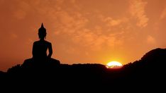 a buddha statue sitting on top of a hill with the sun in the distance behind it