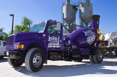 a purple truck is parked in front of some cement mixers and other trucks behind it