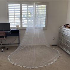 a bed with a white veil on top of it in a bedroom next to a window