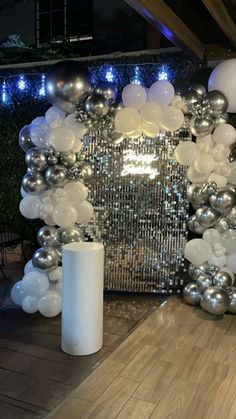 an arch made out of silver and white balloons is displayed in the middle of a room