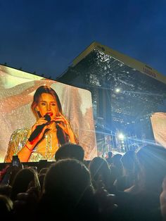 a large screen with a woman on it in the middle of a crowd at an outdoor concert