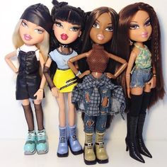 four dolls standing next to each other in front of a white wall and one has her hands on her hips