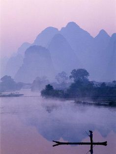 a cross sitting in the middle of a body of water with mountains in the background