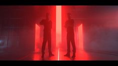 two people standing next to each other in a room with red light coming from them