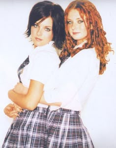 two young women standing next to each other in front of a white wall with their arms crossed