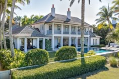 a large white house surrounded by palm trees and greenery next to a swimming pool